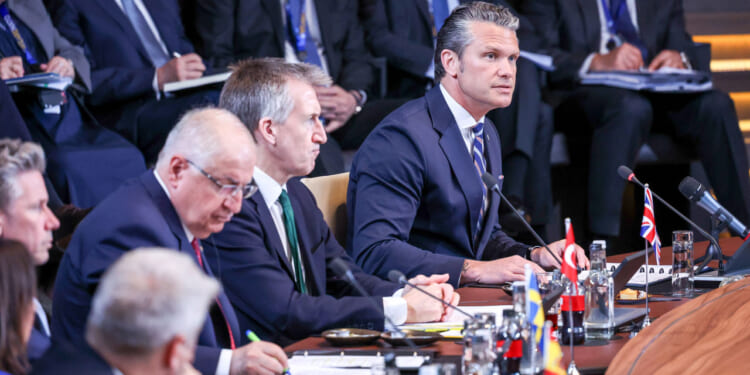 Secretary of War Pete Hegseth speaks while at a table alongside fellow NATO defense ministers.