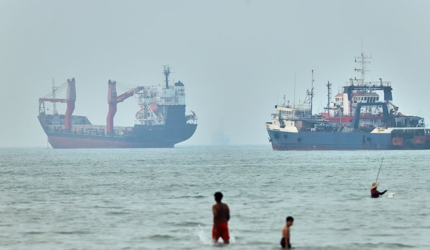 Children wade in the water with cargo ships at anchor in the background and a fisherman nearby, in the Strait of Hormuz off Bandar Abbas, Iran, Tuesday, June 30, 2026. (Amirhosein Khorgooi/ISNA via AP)