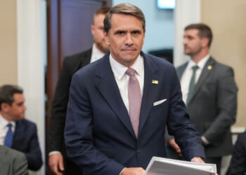 Acting Attorney General Todd Blanche looks right at the camera as he arrives for a hearing with files in his hand.