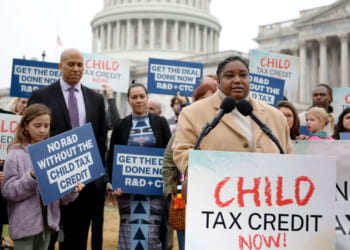 A woman speaks with a "CHILD TAX CREDIT NOW!" sign in front of her and the U.S. Capitol in the background.