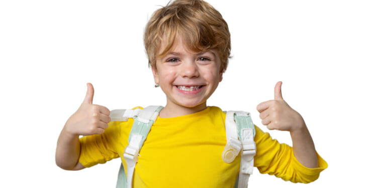 Smiling boy in yellow shirt with backpack over his shoulders gives two thumb's up.