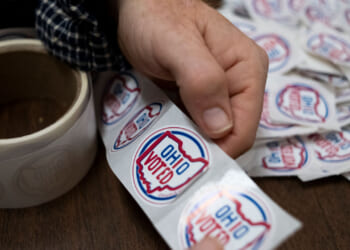 A hand is shown tearing through "Ohio Voted" stickers.