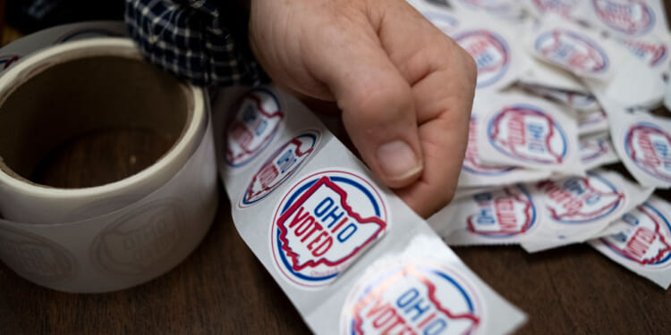 A hand is shown tearing through "Ohio Voted" stickers.