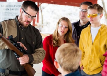 A family watches a gun instructor as he teaches them about a rifle.