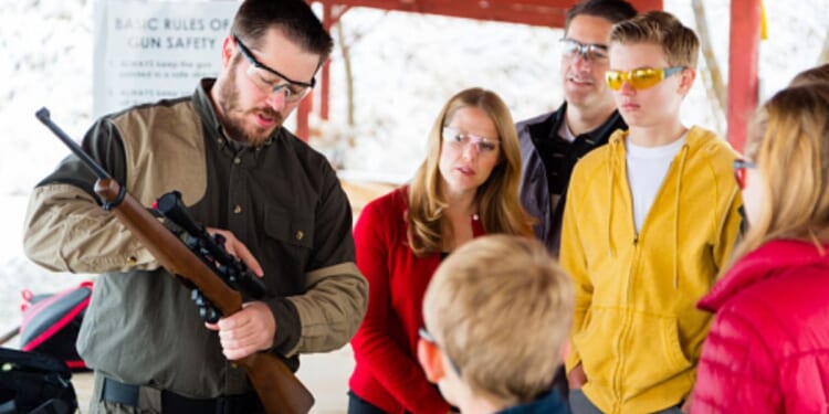 A family watches a gun instructor as he teaches them about a rifle.