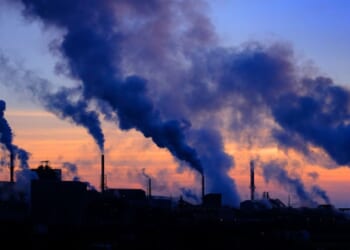 Plumes of smoke cloud from chimneys at dusk.