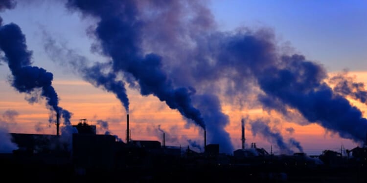 Plumes of smoke cloud from chimneys at dusk.