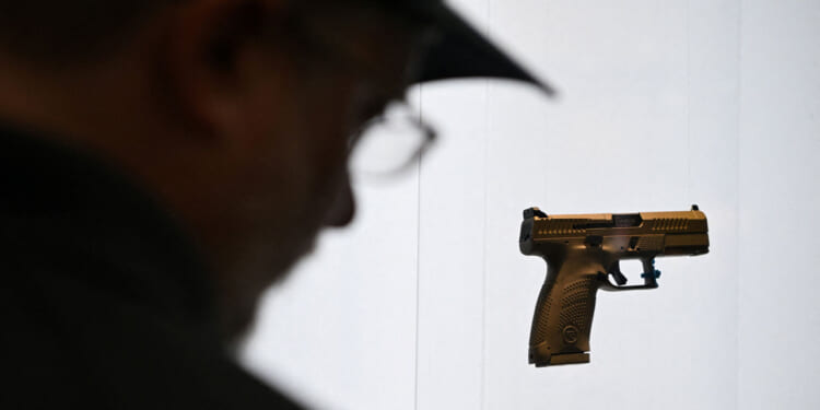 Silhouette of man looking at a display of a handgun against a white background.