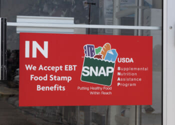A red sign in store door with SNAP logo and "We accept EBT Food Stamp Benefits"