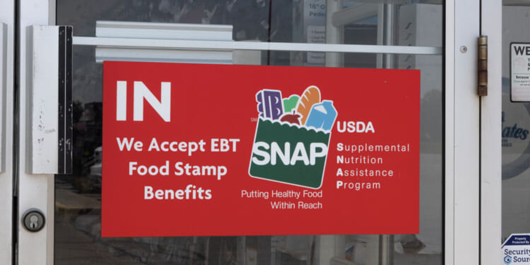 A red sign in store door with SNAP logo and "We accept EBT Food Stamp Benefits"