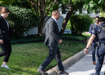 Graham Platner, candidate for Senate, walks in front of a woman companion, with police officers to his side.