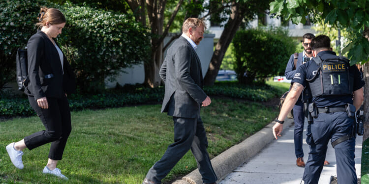 Graham Platner, candidate for Senate, walks in front of a woman companion, with police officers to his side.