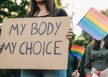 A woman stands with a protest sign with accompanying protesters.