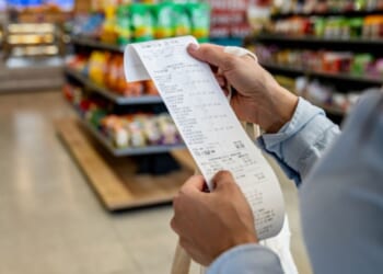 A woman looks at a receipt in a grocery store aisle.