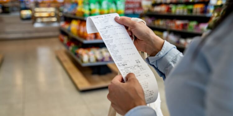 A woman looks at a receipt in a grocery store aisle.