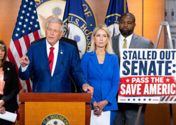 Rep. Ralph Norman of South Carolina Stands at the center of a podium, while other members and a sign urging passage of the SAVE America Act are beside him.