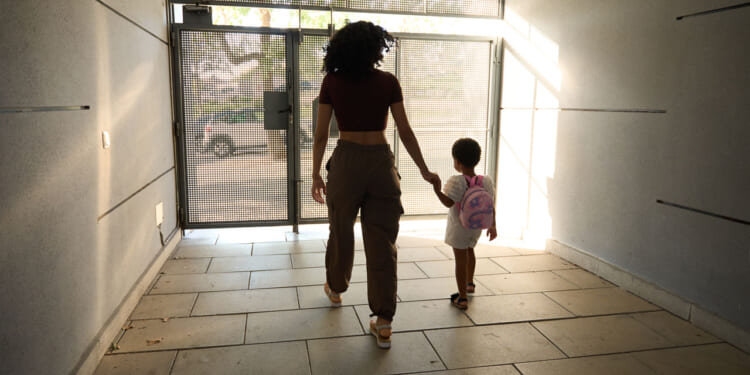 Young black woman leads child toward outside door.