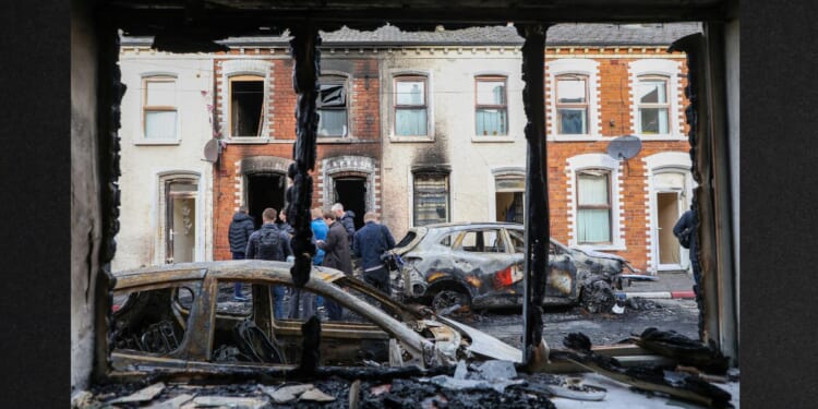 People stand next to burnt-out cars and homes Wednesday after demonstrations turned violent the night before in eastern Belfast, Northern Ireland.