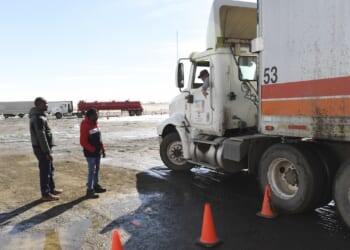 Immigrants stand and look at a truck as they learn how to backup an 18-wheeler.
