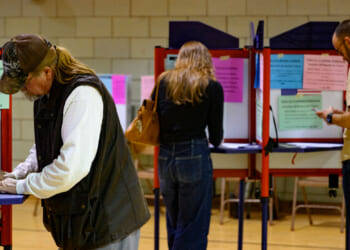 Three people stand at separate voting booths in a room, filling out ballots.