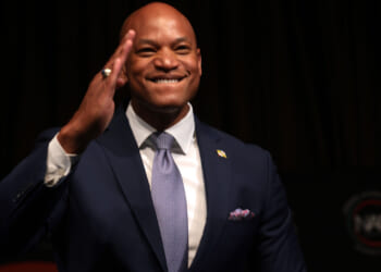 Maryland Gov. Wes Moore raises hand toward forehead as if about to salute.
