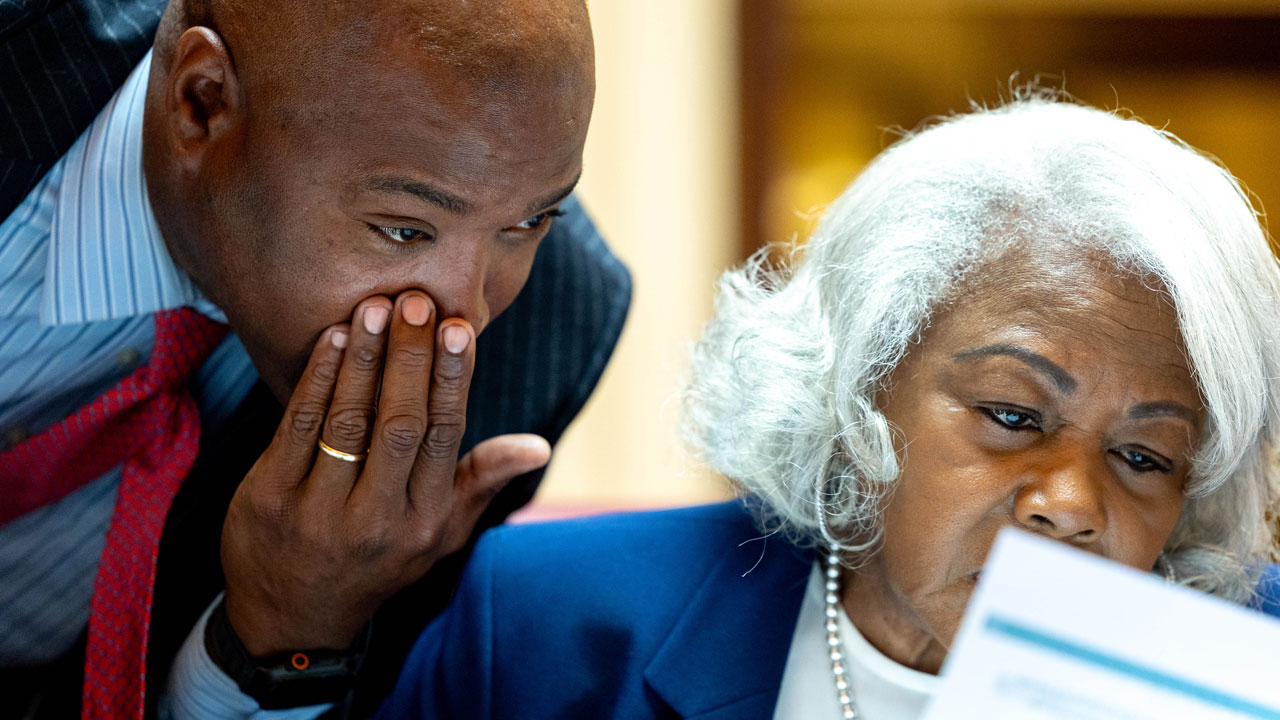 Virginia state Sen. Aaron Rouse covers his mouth as he leans over to talk to Sen. Louise Lucas.