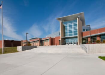 An American school building stands as an American flag waves in the wind.