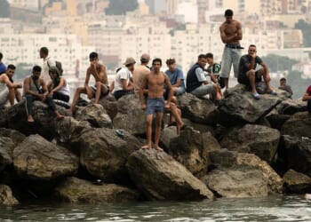 Migrants sit on rocks Friday after swimming through the waters close to the border with Morocco to enter Spain's north Africa's Ceuta enclave. Tens of thousands of migrants crossed overnight from Morocco into Ceuta, a territory with a population of about 80,000, a police source said.