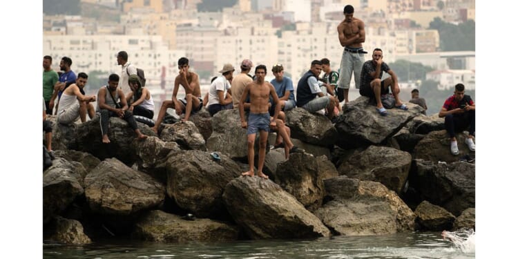Migrants sit on rocks Friday after swimming through the waters close to the border with Morocco to enter Spain's north Africa's Ceuta enclave. Tens of thousands of migrants crossed overnight from Morocco into Ceuta, a territory with a population of about 80,000, a police source said.