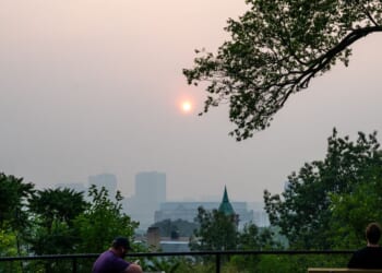 People look on as the sun sets behind a layer of smoke on July 15, 2026, in Minneapolis, Minnesota.