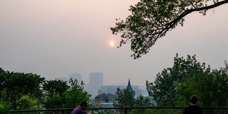 People look on as the sun sets behind a layer of smoke on July 15, 2026, in Minneapolis, Minnesota.