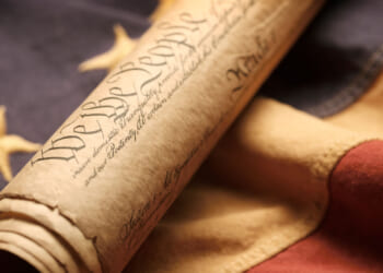 The U.S. Constitution, rolled up, rests on an American flag.