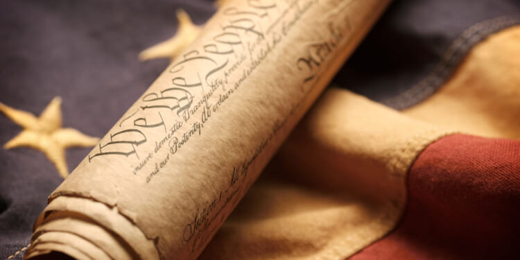 The U.S. Constitution, rolled up, rests on an American flag.