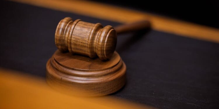A wooden gavel sits on a wooden block on a black suede desk.