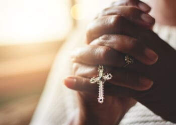 A close-up shot of a woman holding a rosary while praying.