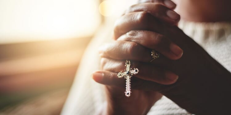 A close-up shot of a woman holding a rosary while praying.