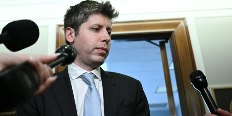 OpenAI CEO Sam Altman is surrounded by microphones, standing in front of an office doorway, appearing to speak or prepare to speak to reporters.
