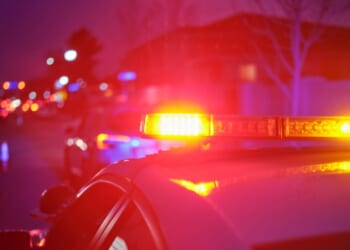 A police car at night alongside a road with emergency lights flashing.