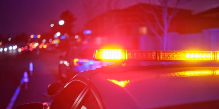 A police car at night alongside a road with emergency lights flashing.