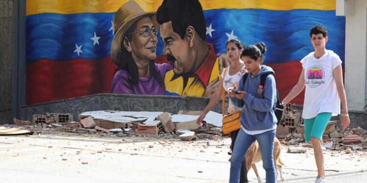 Four people walk past rubble in front of a mural featuring two people, a woman in a hat and a man in yellow, with a Venezuelan flag backdrop.