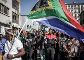 Protesters hold sticks and flags while chanting slogans as they march during a demonstration by the "March & March" and Operation Dudula movements marking an unofficial deadline set by citizen-led groups for undocumented foreign nationals to leave South Africa, in Johannesburg, on June 30, 2026.