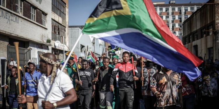 Protesters hold sticks and flags while chanting slogans as they march during a demonstration by the "March & March" and Operation Dudula movements marking an unofficial deadline set by citizen-led groups for undocumented foreign nationals to leave South Africa, in Johannesburg, on June 30, 2026.