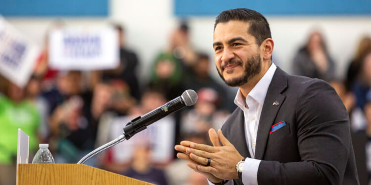 Abdul El-Sayed stands smiling at a podium in a dark suit.