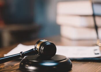 A black wooden gavel sits on a black wooden block in a bright room.