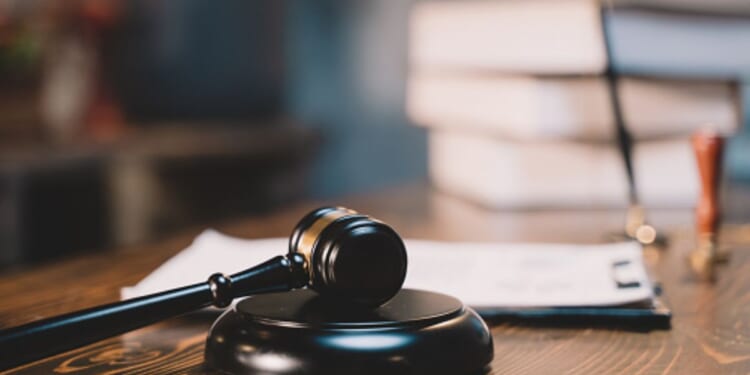 A black wooden gavel sits on a black wooden block in a bright room.
