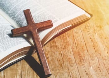 A close-up image of a Christian cross necklace lying against an open Bible.