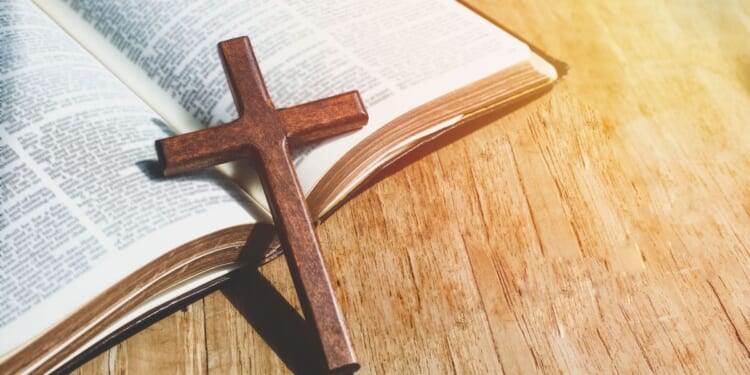 A close-up image of a Christian cross necklace lying against an open Bible.