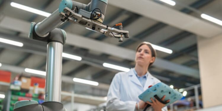 A woman stares at an engineering arm of a machine in a brightly facility.
