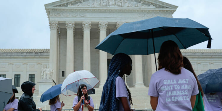 A group of young women stand around the Supreme Court with umbrellas.