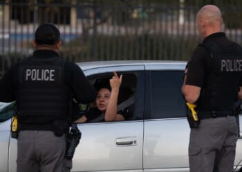 A woman in a car raises her middle finger at two police officers standing outside the vehicle.
